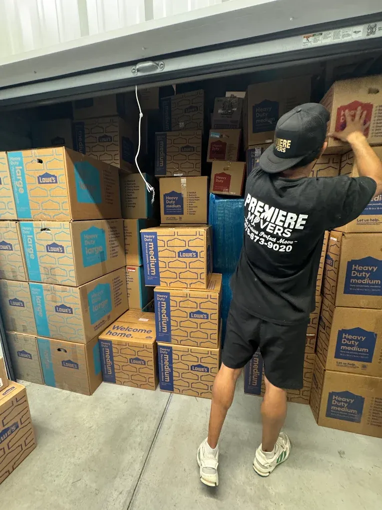 A Premiere Movers crew member in a branded shirt stacking labeled boxes inside a storage unit