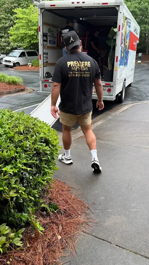 A Premiere Movers crew member walking to a loaded truck with the ramp down outside an apartment building in the rain